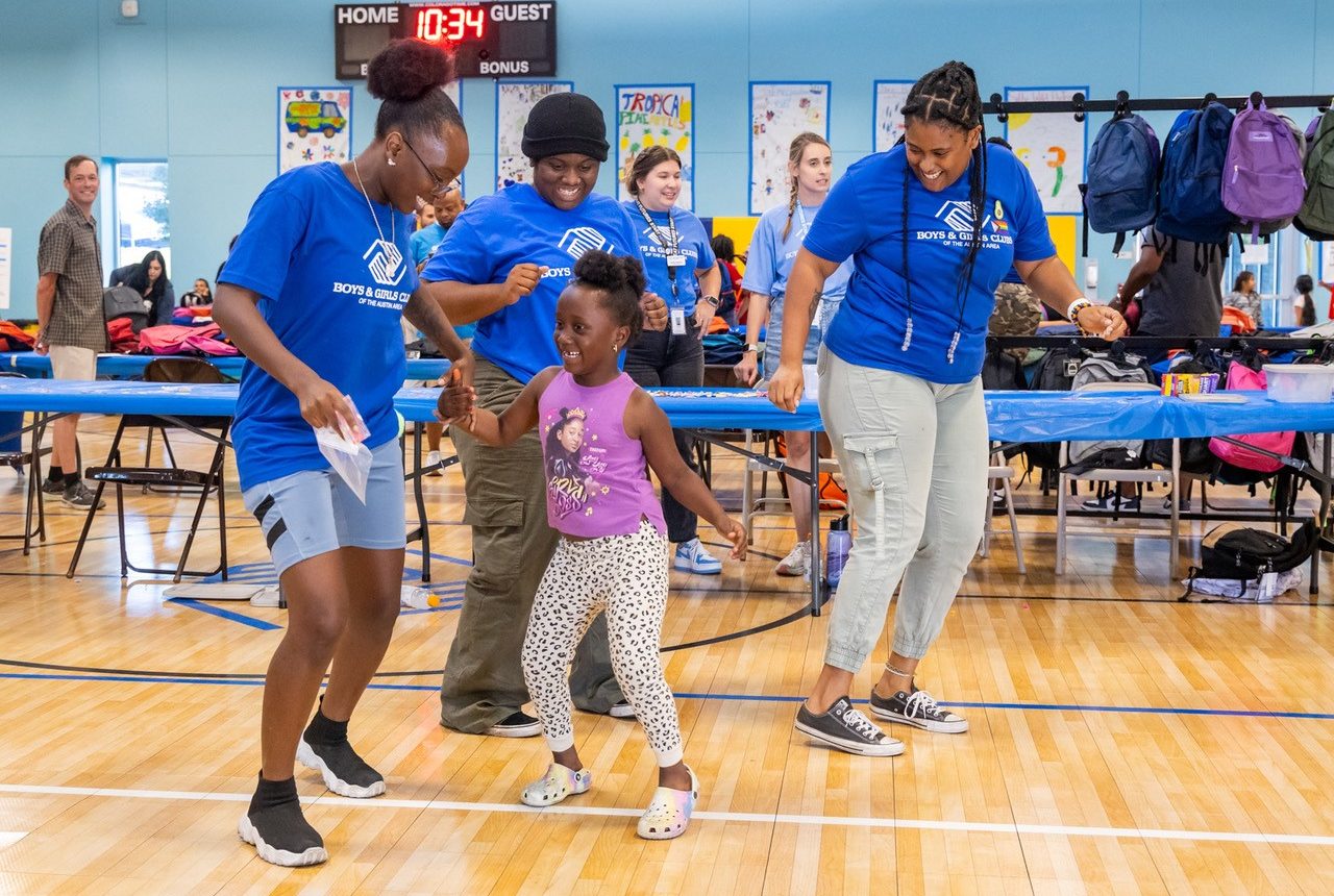 Three Boys & Girls Club staff dance with a young girl at an event